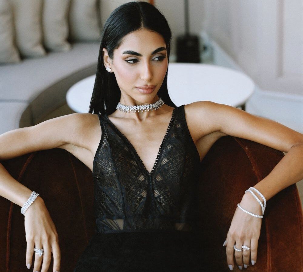 Model seated in a velvet armchair wearing a diamond choker, bracelets and rings