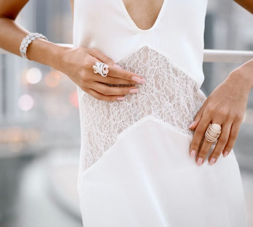 Diamond rings and bracelets worn with hands resting on a white lace dress