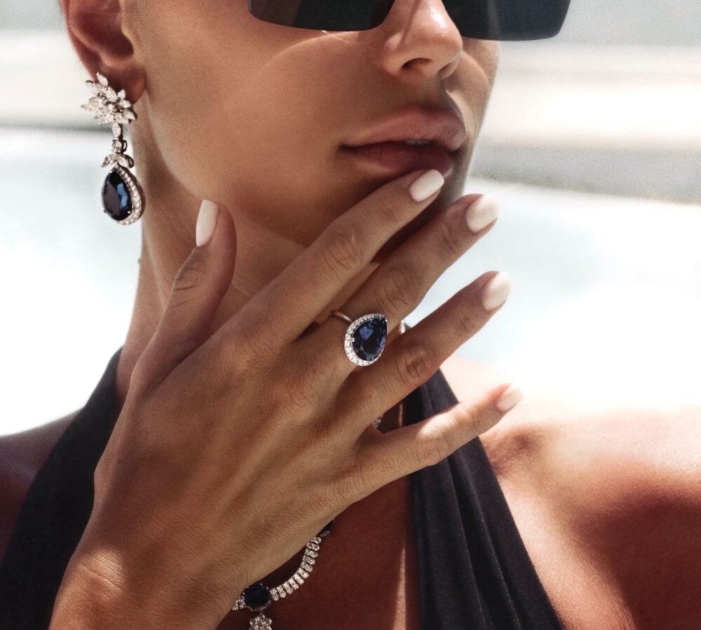 Sapphire pendant necklace, drop earrings and halo ring worn in the sun