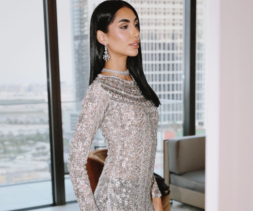 Model in a sequinned gown with diamond choker and chandelier earrings standing by a window