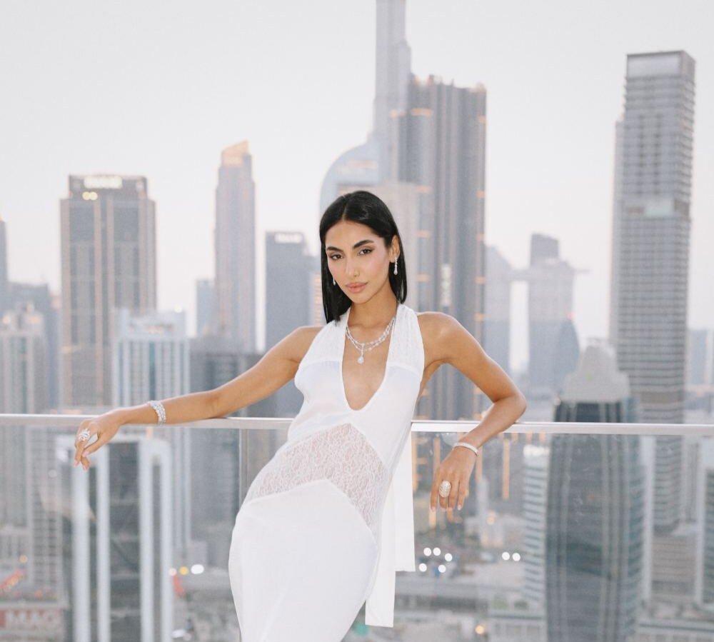 Model in a white lace gown leaning on a terrace railing against the skyline