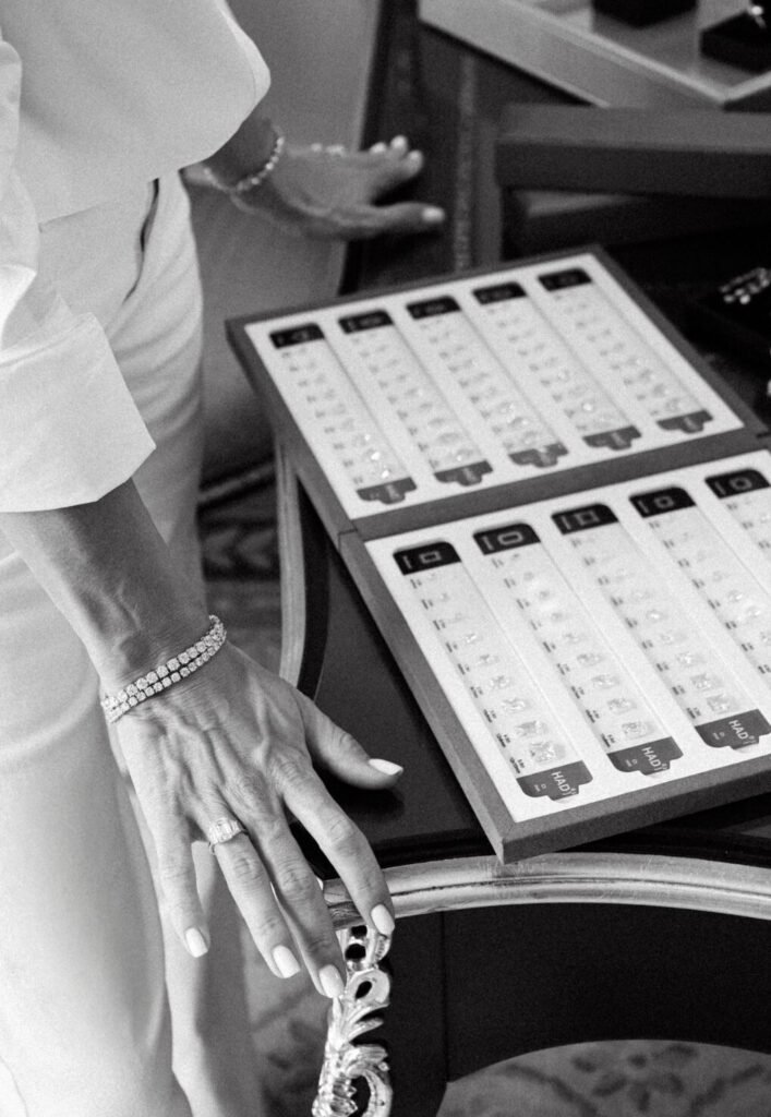 Close view of hands with diamond bracelets and ring beside a tray of certified stones