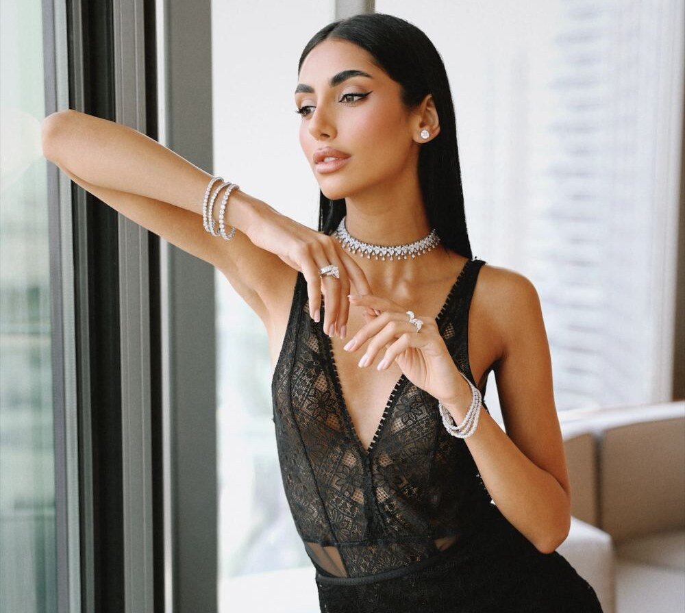 Model in black lace leaning by a window wearing a diamond choker and bracelets
