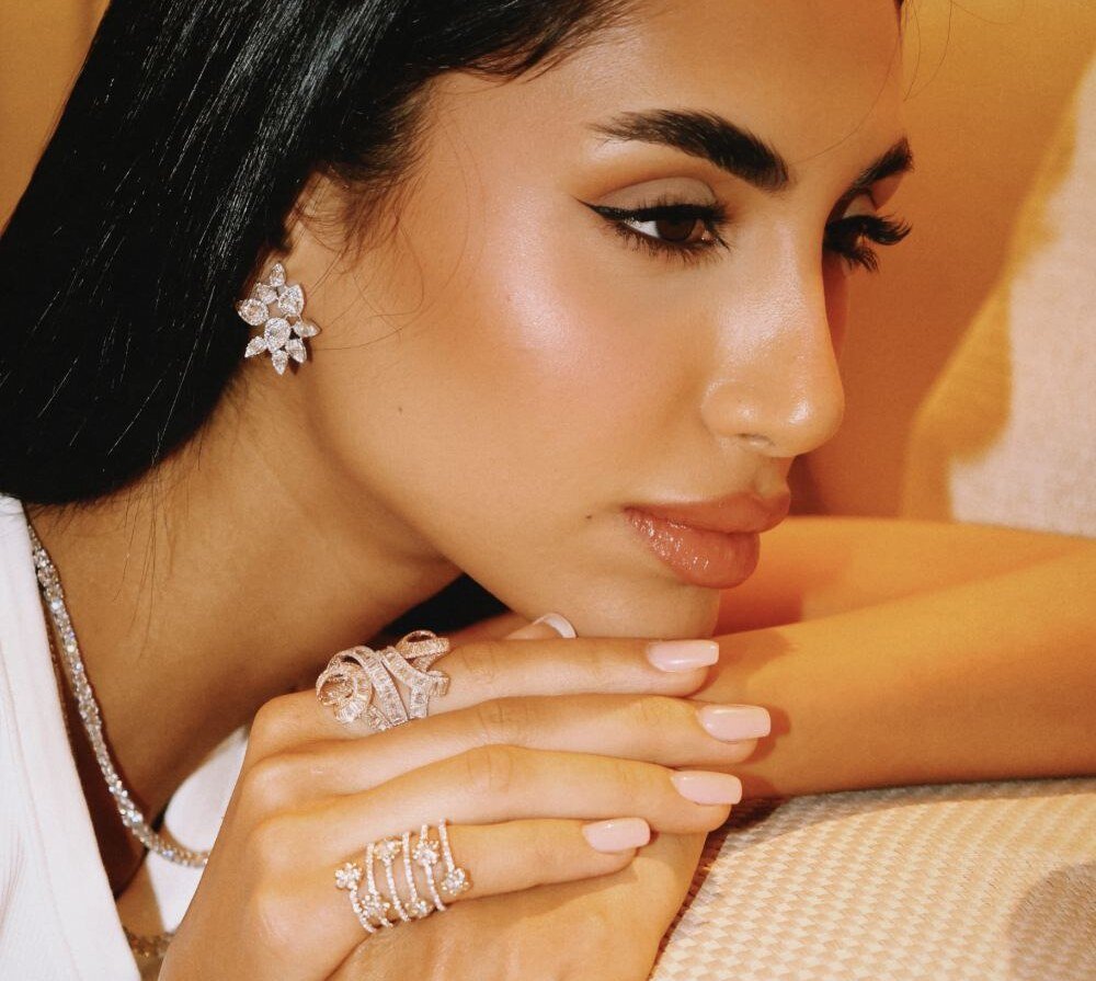 Diamond cluster earrings and cocktail rings worn resting on a sofa arm