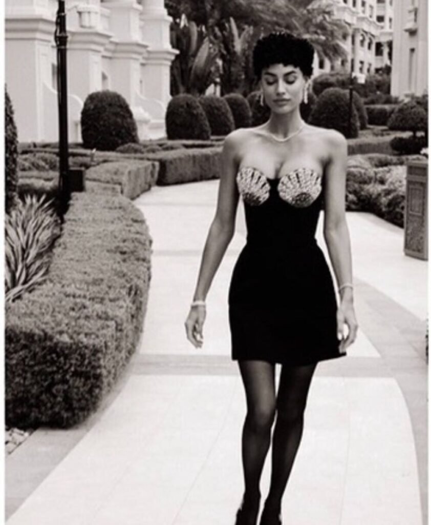 Model in a black cocktail dress walking through manicured gardens